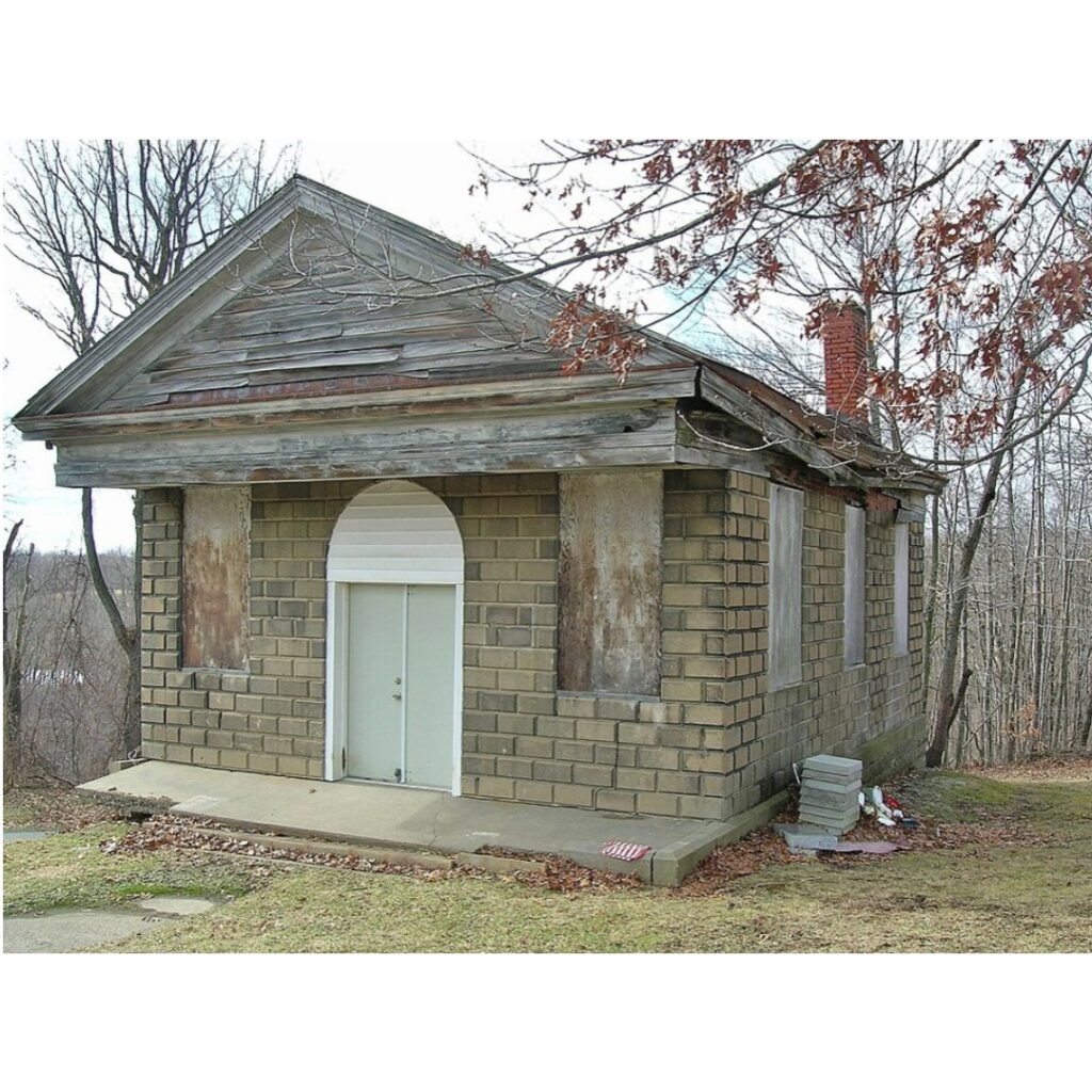 Small historic brick chapel building at Evans City Cemetery, photographed in winter with boarded windows and surrounding trees.