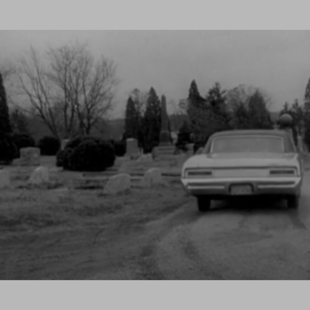 1967 black‑and‑white scene of a car driving up the gravel road inside Evans City Cemetery in the opening of Night of the Living Dead.